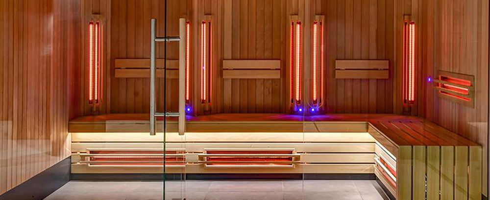 Person relaxing inside a modern full spectrum infrared sauna with soft glowing red and orange lights, highlighting wood interior panels. Infrared heat therapy promotes detoxification, cardiovascular health, and longevity benefits.